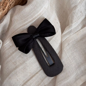 Détail d'une barrette à cheveux avec noeud noir en satin sur un tissu de fond beige doux