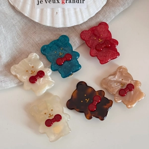 Dettaglio di 6 mollette per capelli a forma di orso colorate con fiocchi rossi su lino