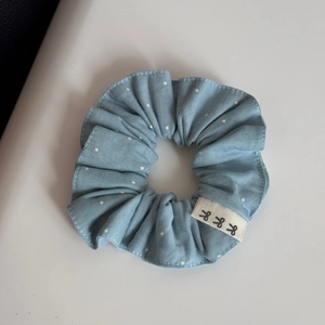 Close-up of light blue polka dot scrunchie with lace trim and bow graphic woven label