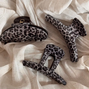 Three-piece leopard print hair claw clips in various shapes on a textured beige fabric