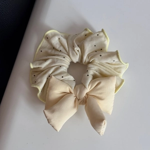 Close-up of cream polka dot scrunchie with large bow and delicate yellow edge stitching