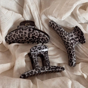 Detailed view of three different leopard print hair claws on a textured beige fabric