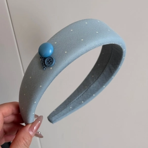 Detailed close-up of blue polka dot headband with handmade tag and button details