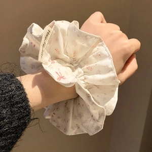 Pink floral scrunchie with handmade label on wrist against soft warm background