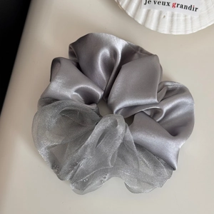 Detail van zilvergrijze scrunchie met satijn en glinsterende mesh op een beige basis
