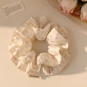 Detailed close-up of a floral scrunchie with pink bows and a handmade textile label