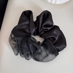Detailweergave van zwarte satijnen en sprankelende organza scrunchie met glitter