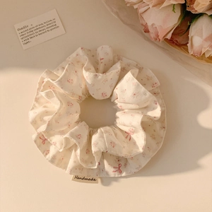 Detail shot of a handmade floral scrunchie with pink bow patterns and a woven label