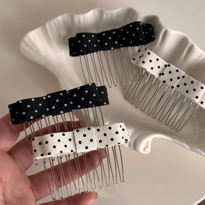 Close-up of black and white polka dot bow hair combs on a white shell tray