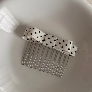 Detail of a white polka dot bow hair comb with silver metal prongs on white ceramic