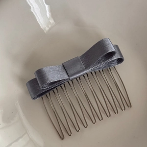 Dettaglio macro del fiocco in raso grigio fissato su un pettine per capelli in metallo