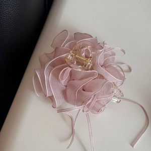 Détail d'une pince à cheveux fleur en mousseline rose avec bords pailletés et ressort doré