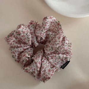 Detailed macro view of a floral chiffon hair scrunchie with a black fashion label tag