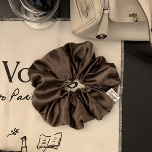 Detailansicht eines Schokoladen-Satin-Scrunchies mit Premium-Marken-Logo-Etikett