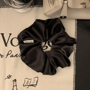 Detailansicht des luxuriösen schwarzen Satin-Haargummis mit Seidenglanz und weißem Etikett