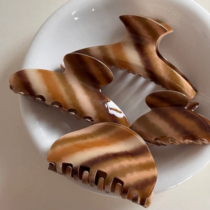Detail view of four amber marble hair claws made of high-gloss acetate in a white ceramic dish