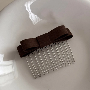 Close-up of a dark brown fabric bow hair comb with ten silver metal teeth on a white surface