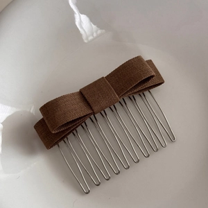 Detailed macro view of a brown fabric bow hair comb with 10 silver metal teeth for styling