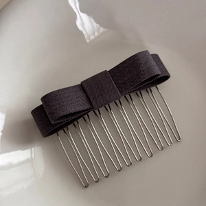 Detailed view of a dark grey bow hair comb with 12-tooth metal clip on ceramic background