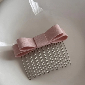 Detail of a sweet pink satin bow hair comb with silver metal teeth for styling