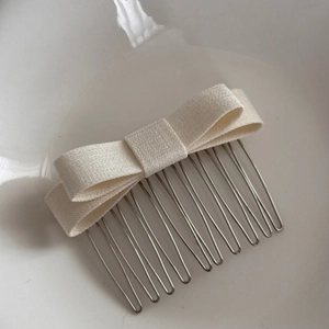 Close-up of cream white fabric bow hair comb with stable silver metal teeth for styling