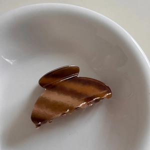 Detailed close-up of amber tortoiseshell hair claw clip in a white ceramic dish