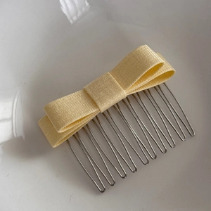 Close-up of a pale yellow ribbon bow hair comb with polished silver metal teeth
