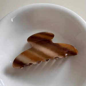 Detailed view of glossy dark brown gradient hair claw clip in a white ceramic bowl