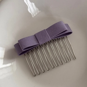 Detailed close-up of a purple fabric bow hair comb with ten silver metal teeth