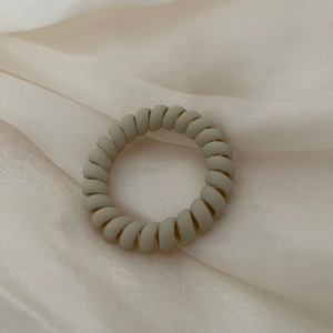 Minimalist matte beige spiral hair tie on a luxurious cream silk background texture