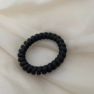 Close-up of matte black spiral telephone wire hair tie on beige silk fabric background