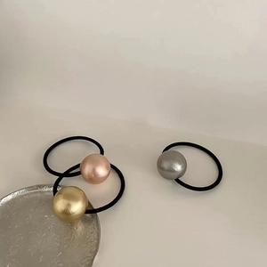 Detailed shot of three metallic sphere hair ties in gold and silver on a textured tray