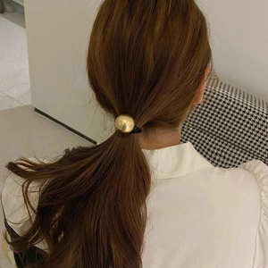 Close-up of minimalist golden metal sphere elastic hair tie on a low ponytail