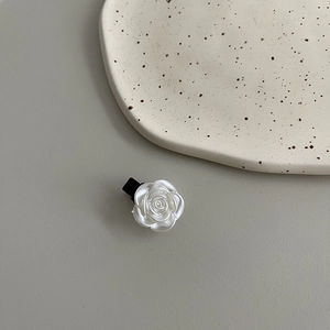 Détail d'une pince à cheveux en forme de rose blanche en résine avec un petit clip noir
