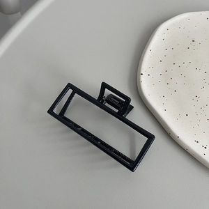 Detail view of a minimalist black square metal hair claw clip with a glossy finish