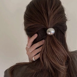 Detailed view of silver metallic ball hair tie on ponytail with minimalist rings