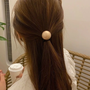 Close-up of a minimalist black elastic hair tie with a large champagne gold pearl bead