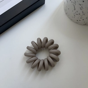 Minimalist matte grey spiral telephone cord hair tie on a clean aesthetic background