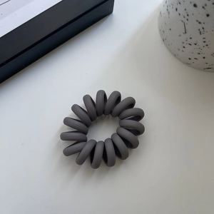 Close-up of matte dark grey spiral hair tie with frosted texture on white table