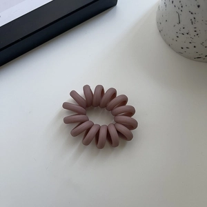 Close-up of matte spiral hair tie in dusty rose pink on a minimalist white surface