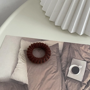 Gros plan sur un élastique à cheveux spirale marron floqué en velours et plastique souple