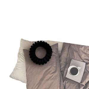 Élastique à cheveux spirale noir minimaliste avec finition mate sur un coussin décoratif