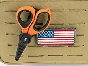 Tactical orange EMT shears with black blades mounted on a sand-colored MOLLE panel vest