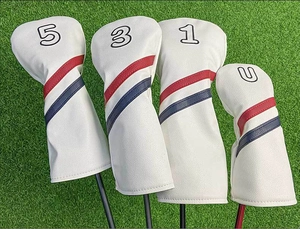 Dettaglio set coprimazze da golf bianchi con strisce rosse e blu su prato sintetico