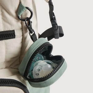 Close-up of a mini green pacifier pouch with metal hook attached to a backpack