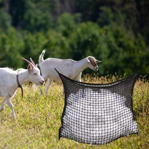 Durable black woven mesh hay net for horses and goats on a farm pasture background