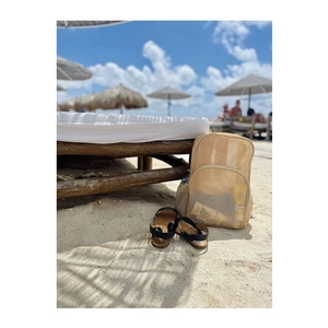 Beige mesh backpack and black sandals on beach sand with summer vacation background