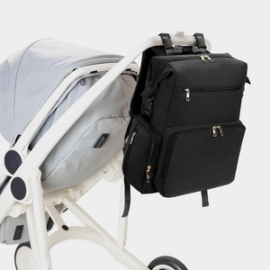 Black waterproof diaper backpack with gold zippers hanging on a white stroller