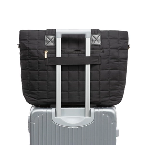Grand sac fourre-tout matelassé noir fixé sur la poignée d'une valise de voyage