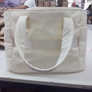 Detail of quilted puffer tote bag in off-white showing wide straps and side pocket